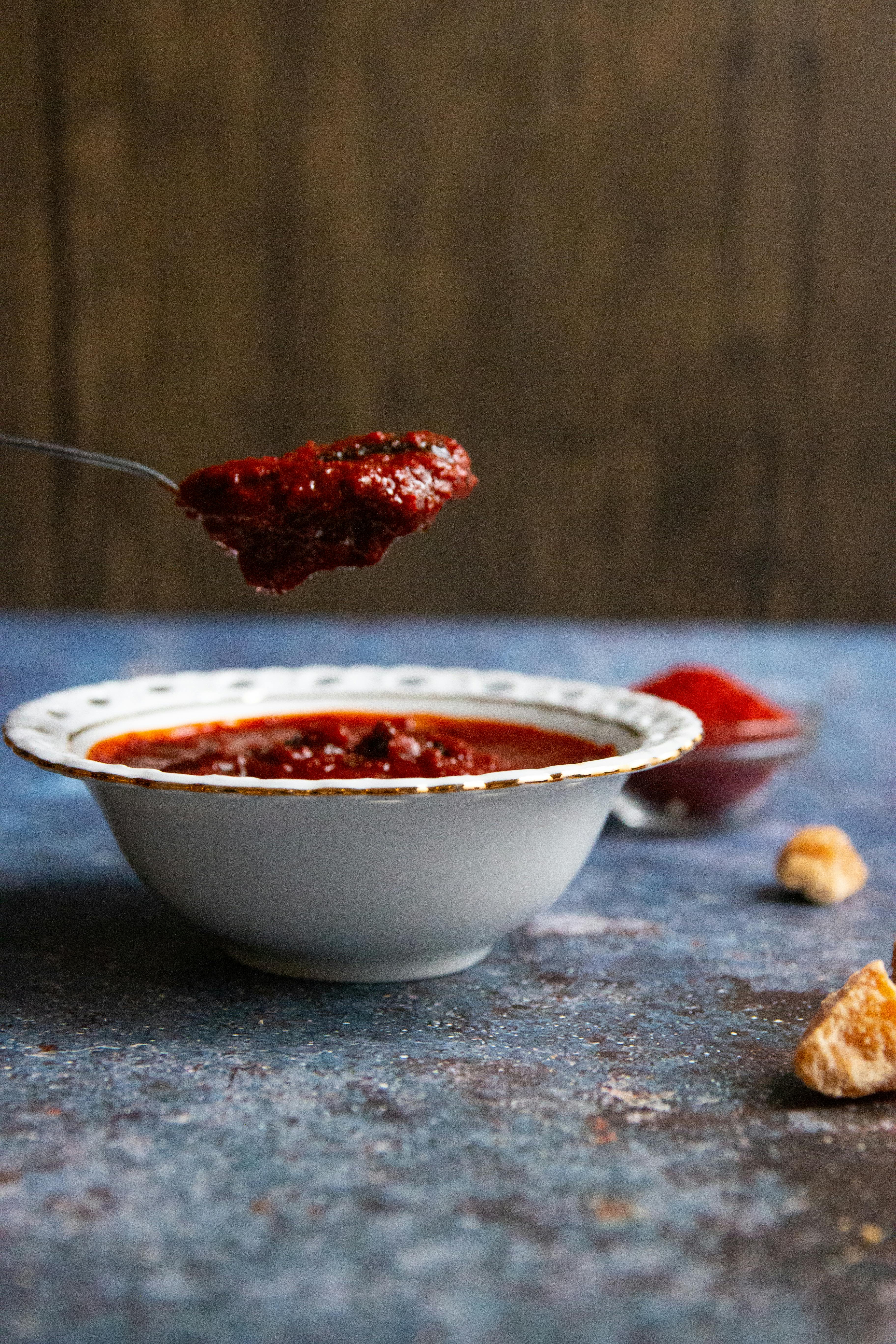 Close-up of a spicy red sauce in a bowl with a spoonful lifting the condiment, showcasing its texture.
